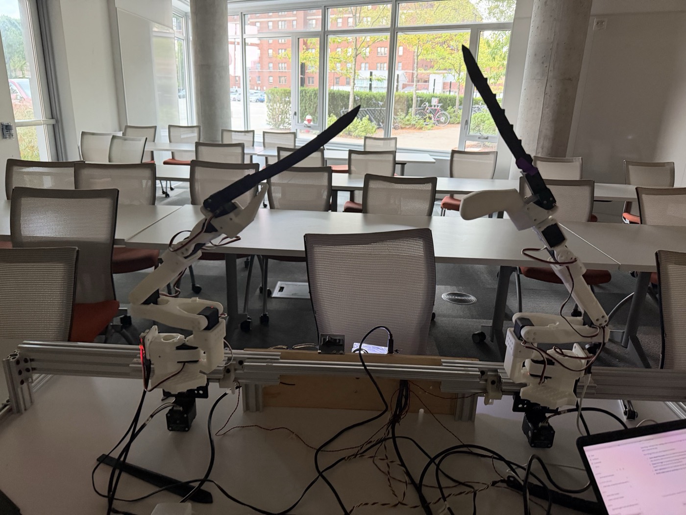 Two robot arms on a rail, both blades raised en garde, in a classroom
